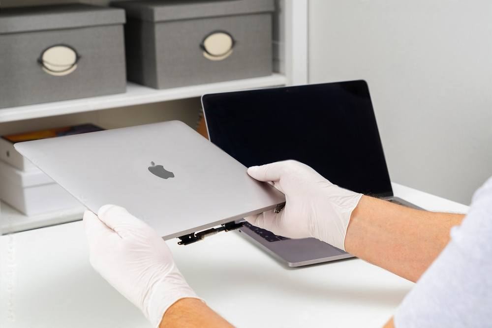 Gloved hands separating a MacBook display assembly from its body