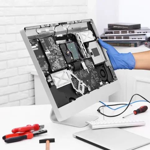 A gloved hand working inside an opened iMac on a bench