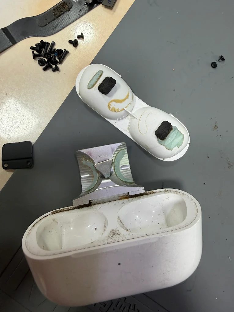 An AirPods Pro charging case opened up, the lid and hinge separated, with dirt and residue inside