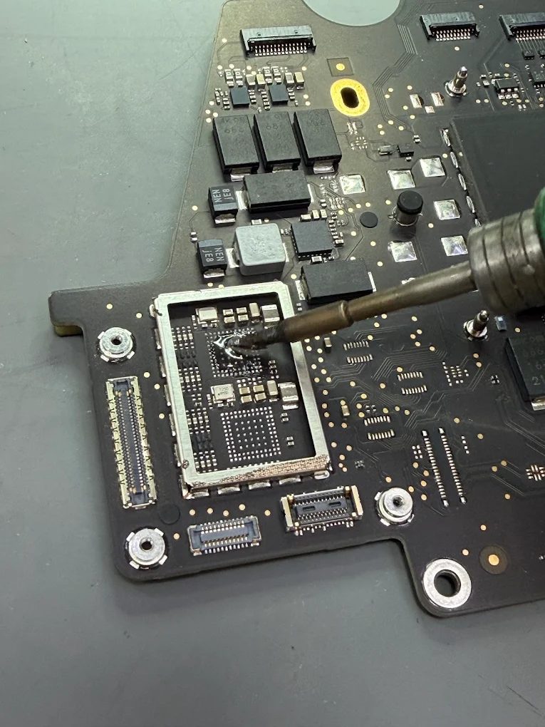A soldering iron working inside the frame of a removed shield on a MacBook logic board